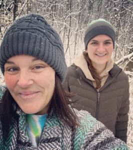 Tina and Monica hiking in the woods with snow covering the branches.