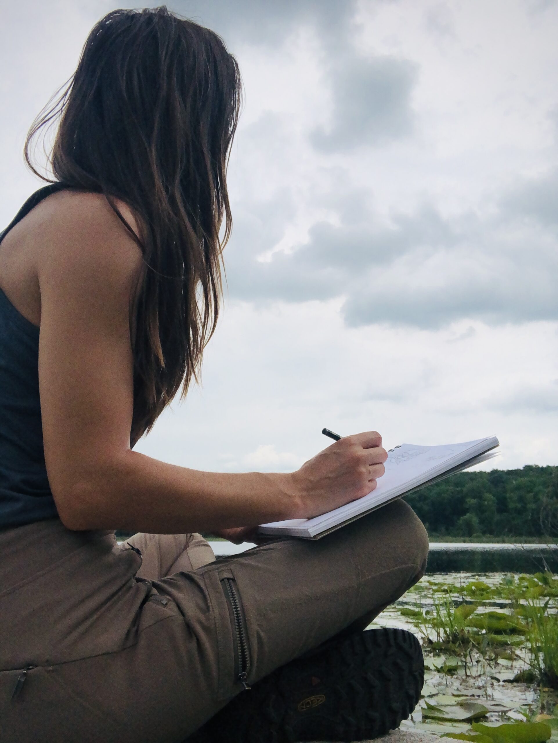 Rebecca sitting by Little Gentian Lake and looking out at the water with a sketchpad in hand